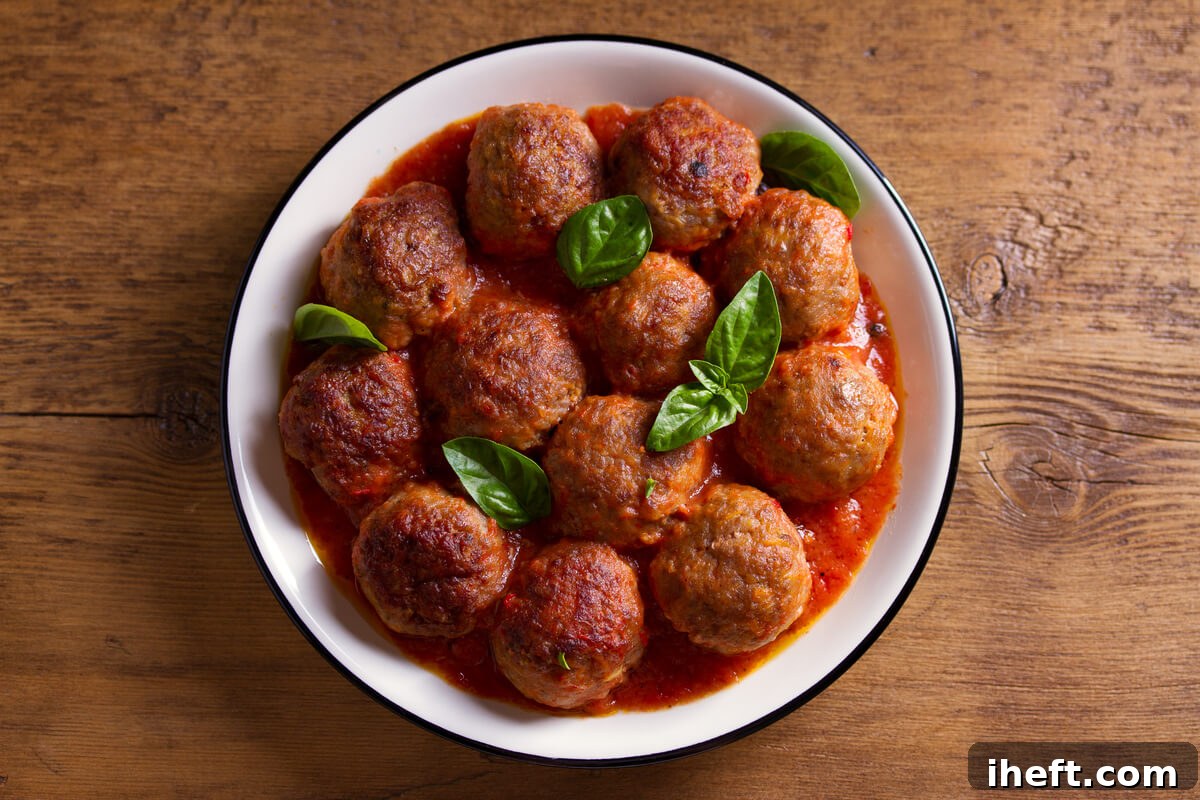 A white bowl filled with authentic Italian meatballs bathed in a rich tomato sauce, garnished with fresh basil leaves, resting on a rustic wooden table.
