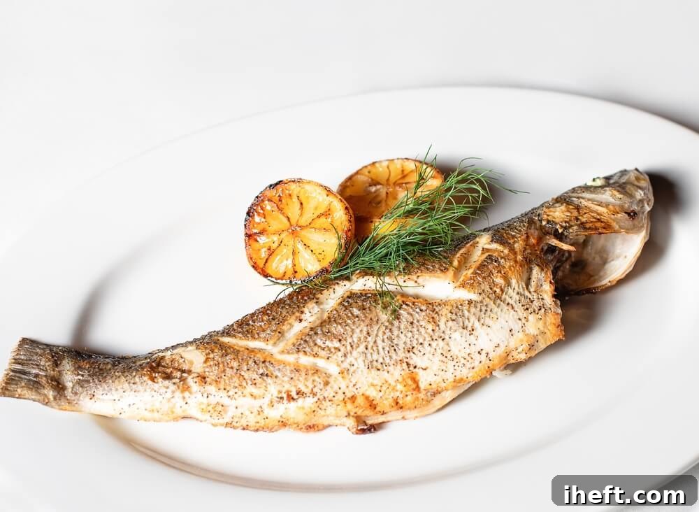 A perfectly roasted whole Branzino fish presented on a white plate, garnished with vibrant lemon halves and fresh dill, ready to be enjoyed.