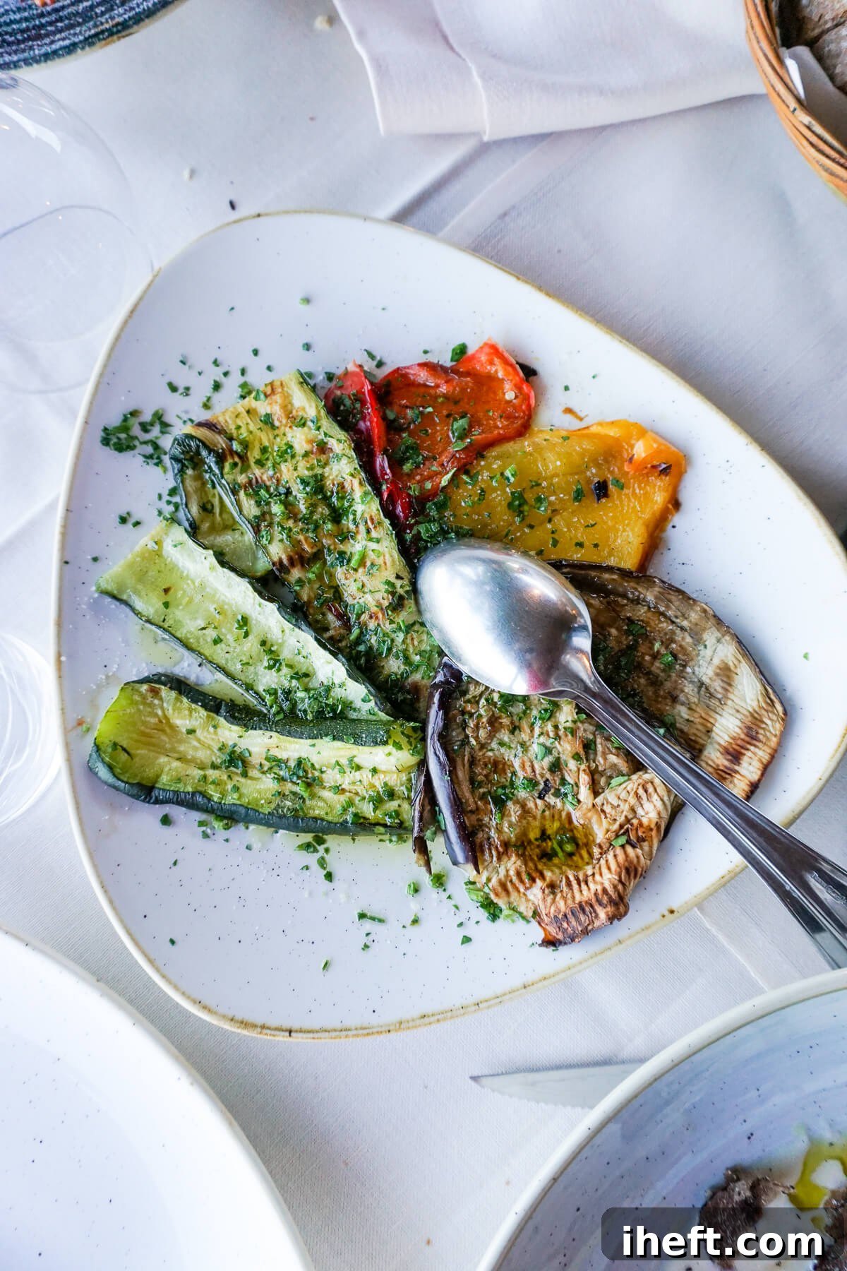 A rectangular white platter artfully arranged with colorful grilled zucchini, eggplant, and bell peppers, set on a white tablecloth-covered table in Tuscany.