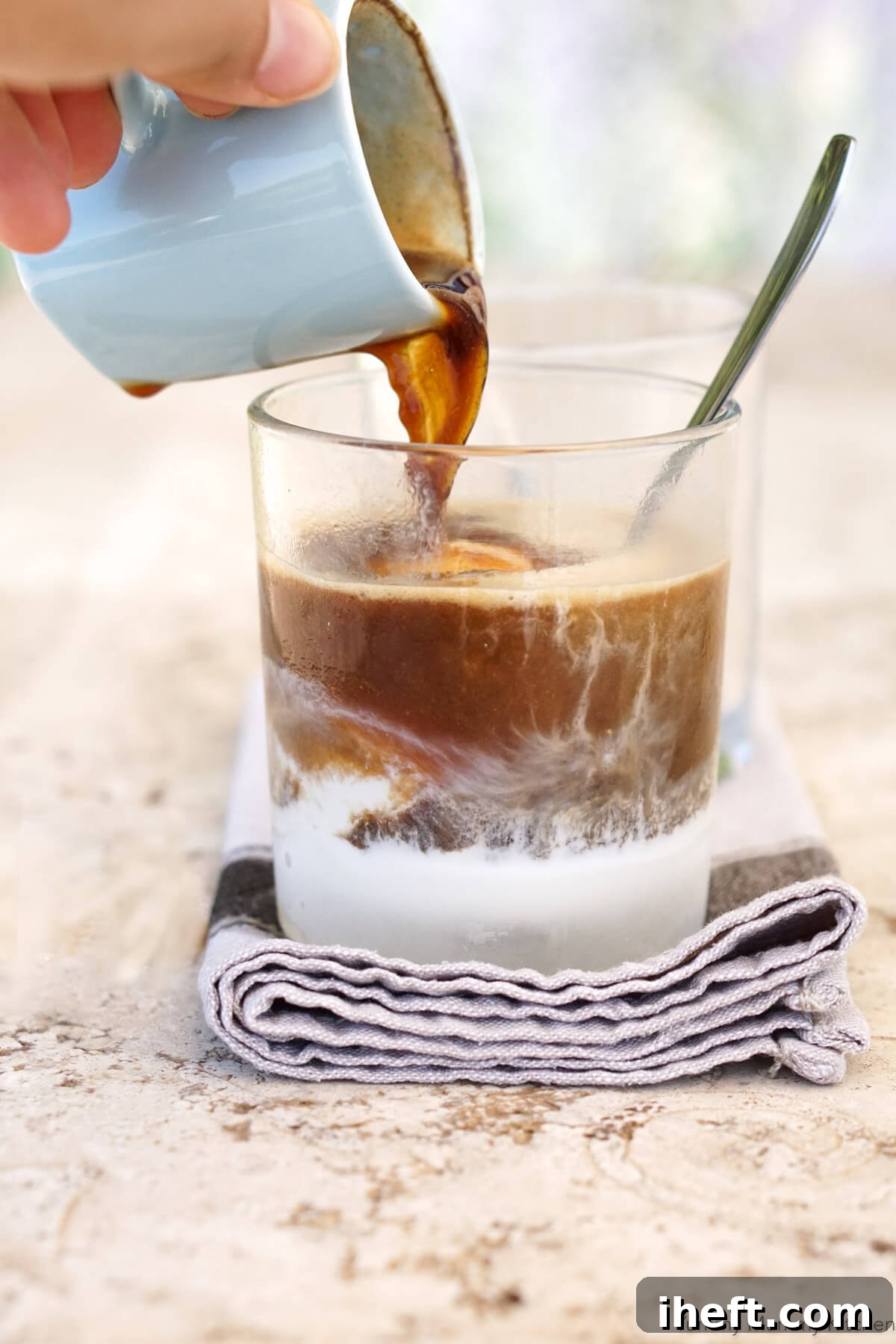 A hand gracefully pours a steaming shot of espresso over a scoop of vanilla ice cream, creating a classic Affogato, an exquisite Italian dessert.