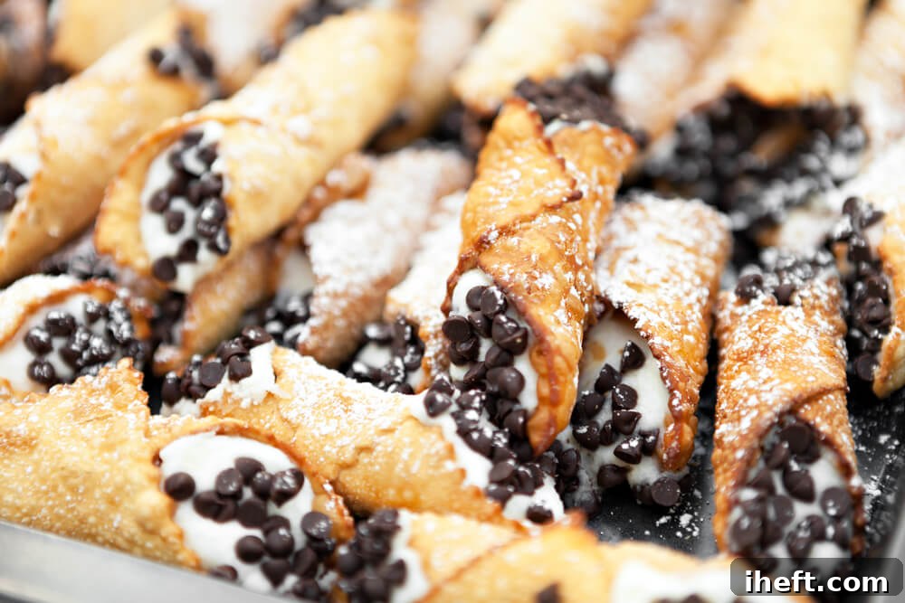 A delightful pile of cannoli, generously garnished with chocolate chips and dusted with powdered sugar, ready to be enjoyed.