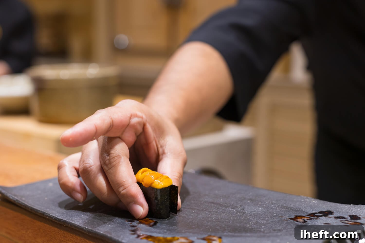 A sushi chef places a piece of uni (sea urchin) sushi on black plate. 