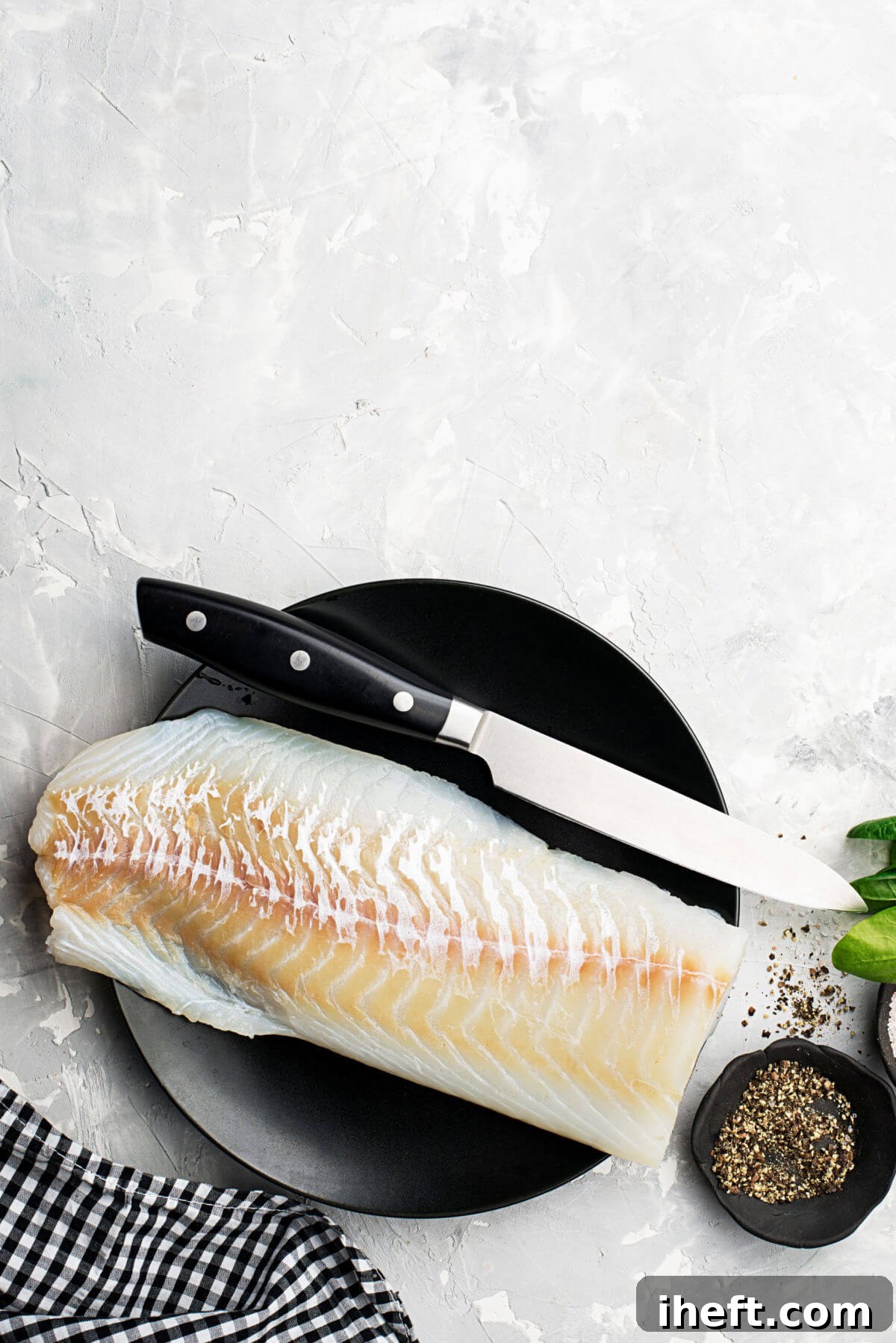 A large black cod (sablefish) filet on a black plate with a chef's knife.