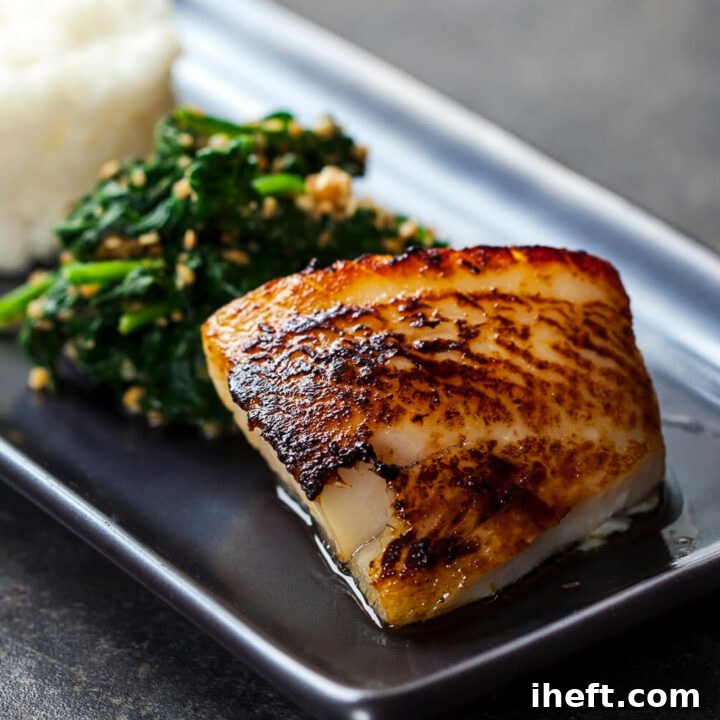 A filet of miso black cod served with spinach and rice on a black plate.