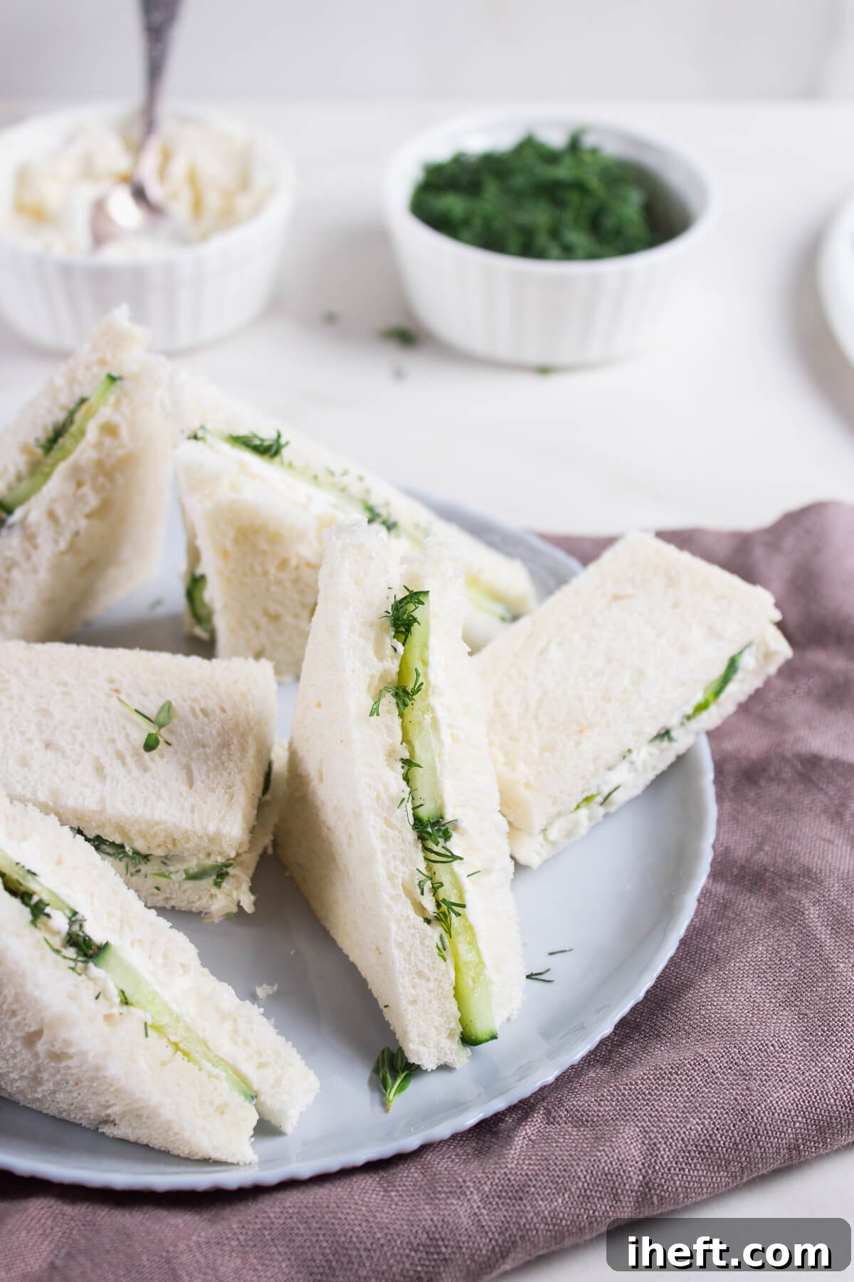 Delicate cucumber, cream cheese, and herb sandwiches, precisely cut into triangles and arranged on an elegant grey plate.