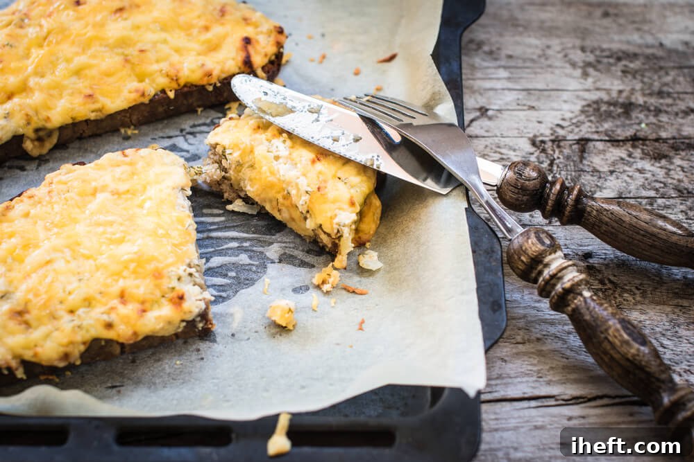 Two golden slices of Welsh Rarebit, a traditional British cheese toast, meticulously placed on a parchment-lined cookie sheet.