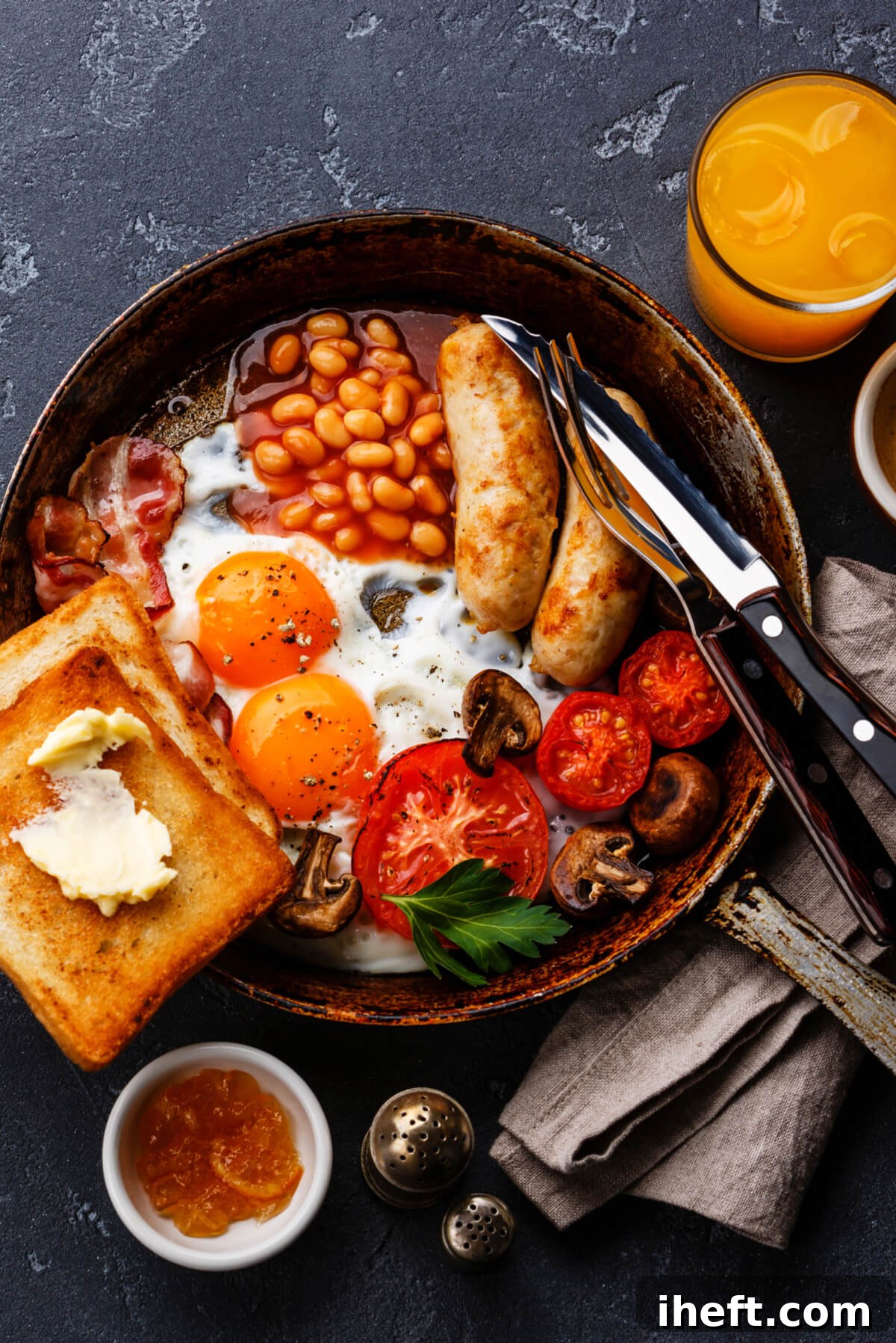 A skillet brimming with a full English breakfast, featuring baked beans, savory sausages, perfectly fried eggs, grilled tomatoes, sautéed mushrooms, and crisp toast.