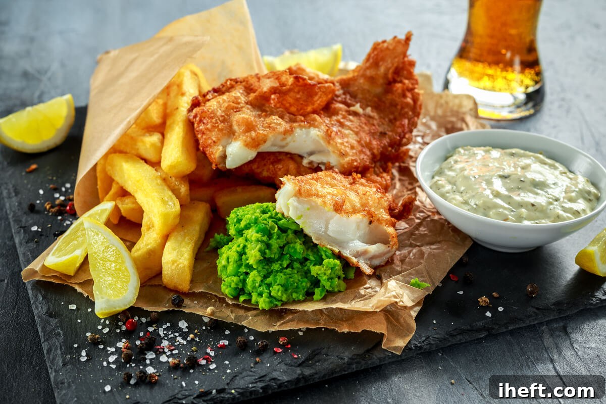 A classic British fish and chips, presented on parchment paper, accompanied by a side of vibrant mushy peas and creamy tartar sauce.