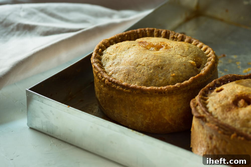 Two individual steak and kidney pies, or British pot pies, arranged on a silver baking sheet, illustrating a savory British food tradition.