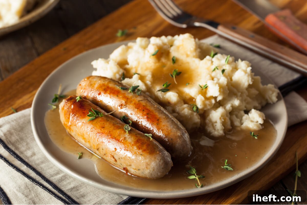 A ceramic plate elegantly topped with Bangers and Mash, a traditional British food composed of two savory sausages, creamy mashed potatoes, and rich gravy.