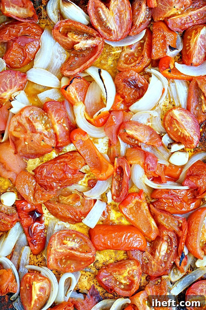 A sheet pan filled with fresh tomatoes, onions, garlic, and bell pepper, ready for roasting to make a savory tomato soup.