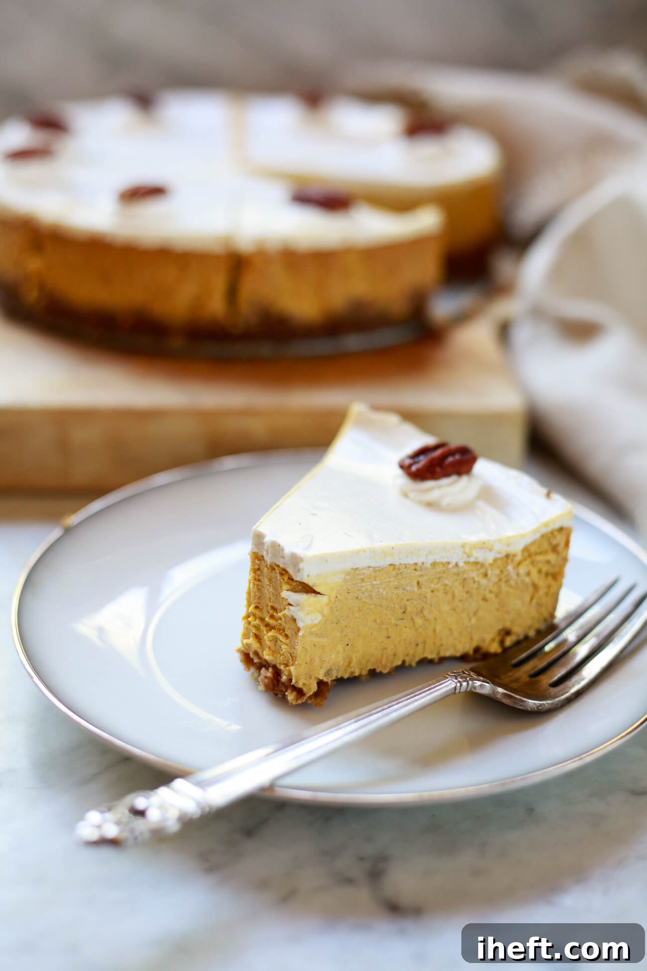 A perfectly sliced homemade pumpkin pie cheesecake elegantly presented on a white plate, showcasing its creamy texture and distinct layers. A delightful autumnal dessert.