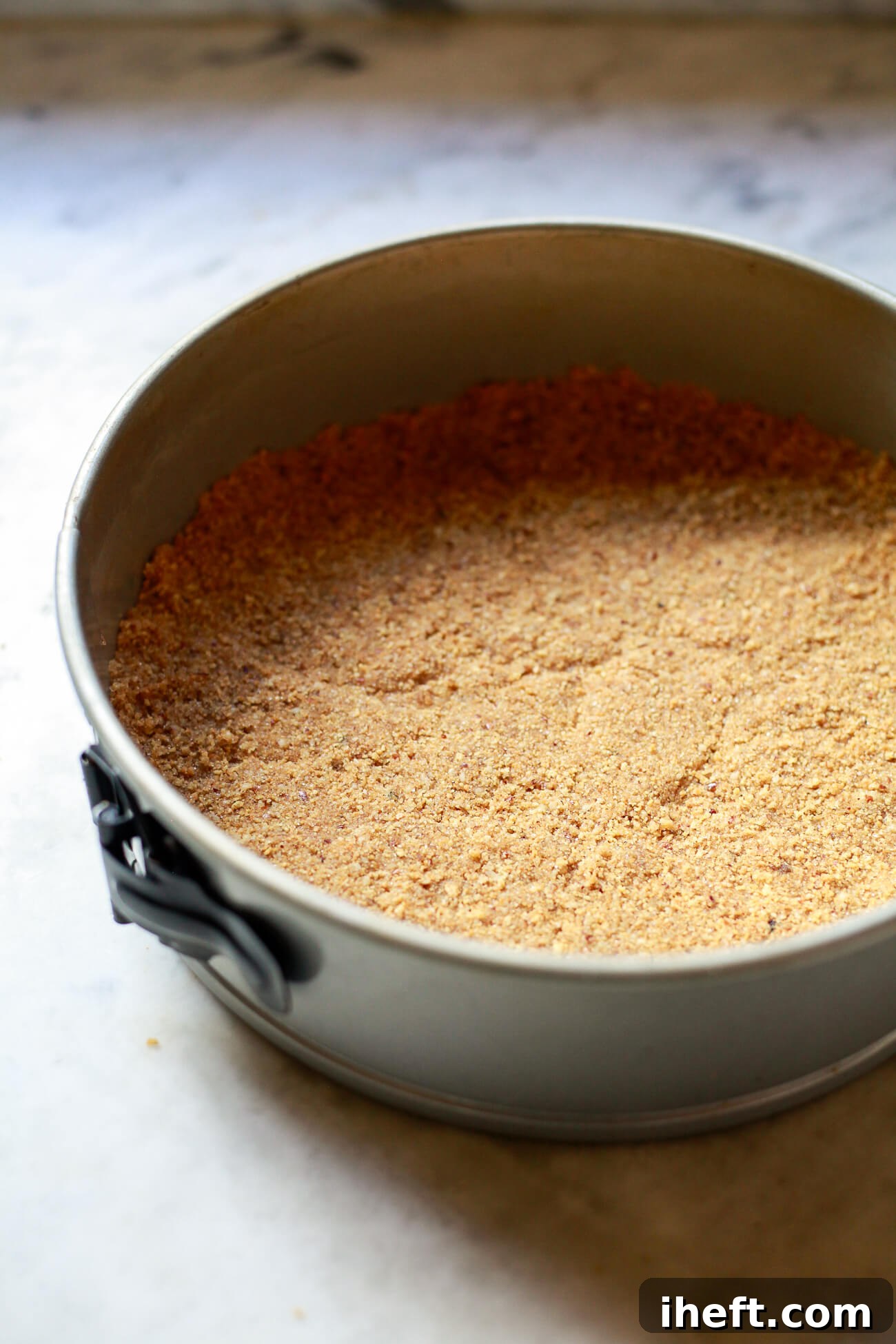 A perfectly pressed graham cracker and pecan crust in a springform pan, ready for the pumpkin cheesecake filling.