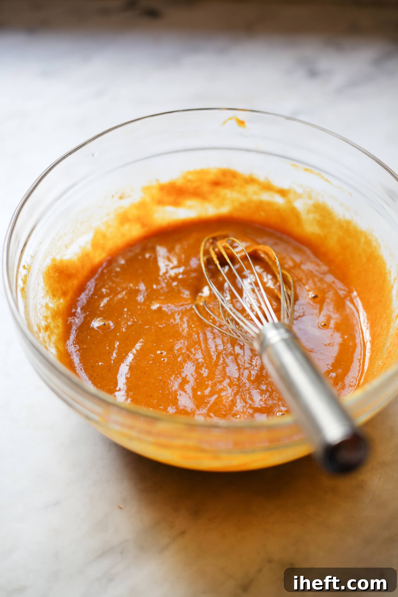 A glass bowl containing the vibrant orange pumpkin puree mixture for the cheesecake filling, infused with aromatic fall spices.