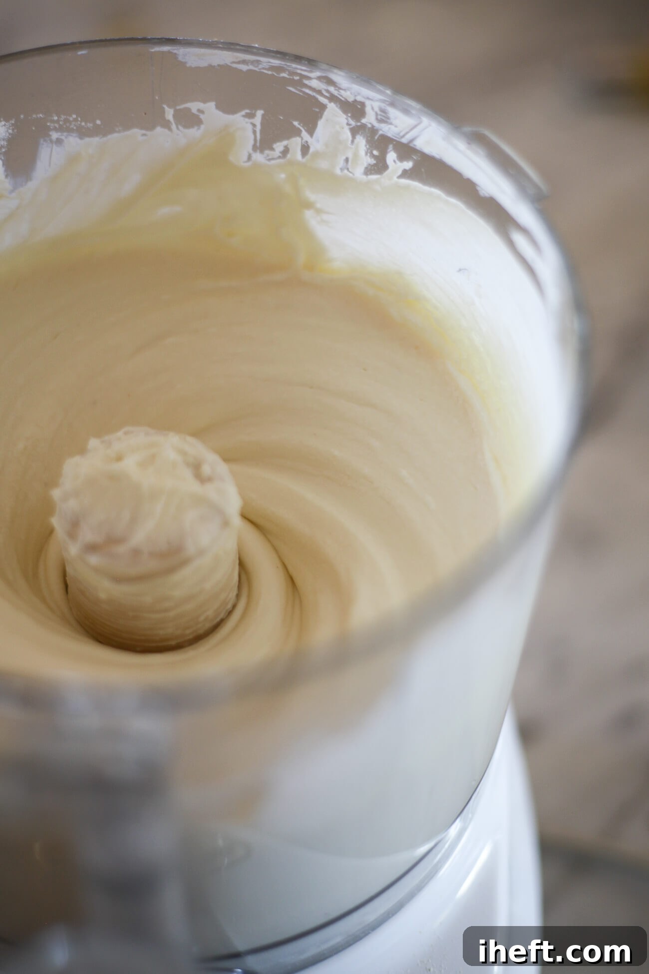 A food processor vigorously mixing softened cream cheese and granulated sugar, forming the smooth, creamy base for the cheesecake.