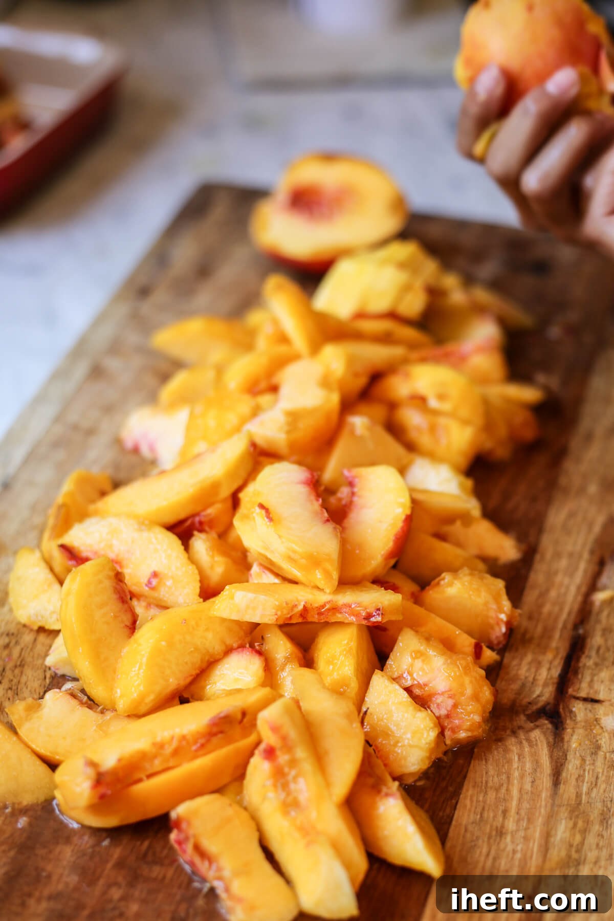A pile of peeled and sliced peaches ready for a delicious peach crisp on a wooden cutting board.