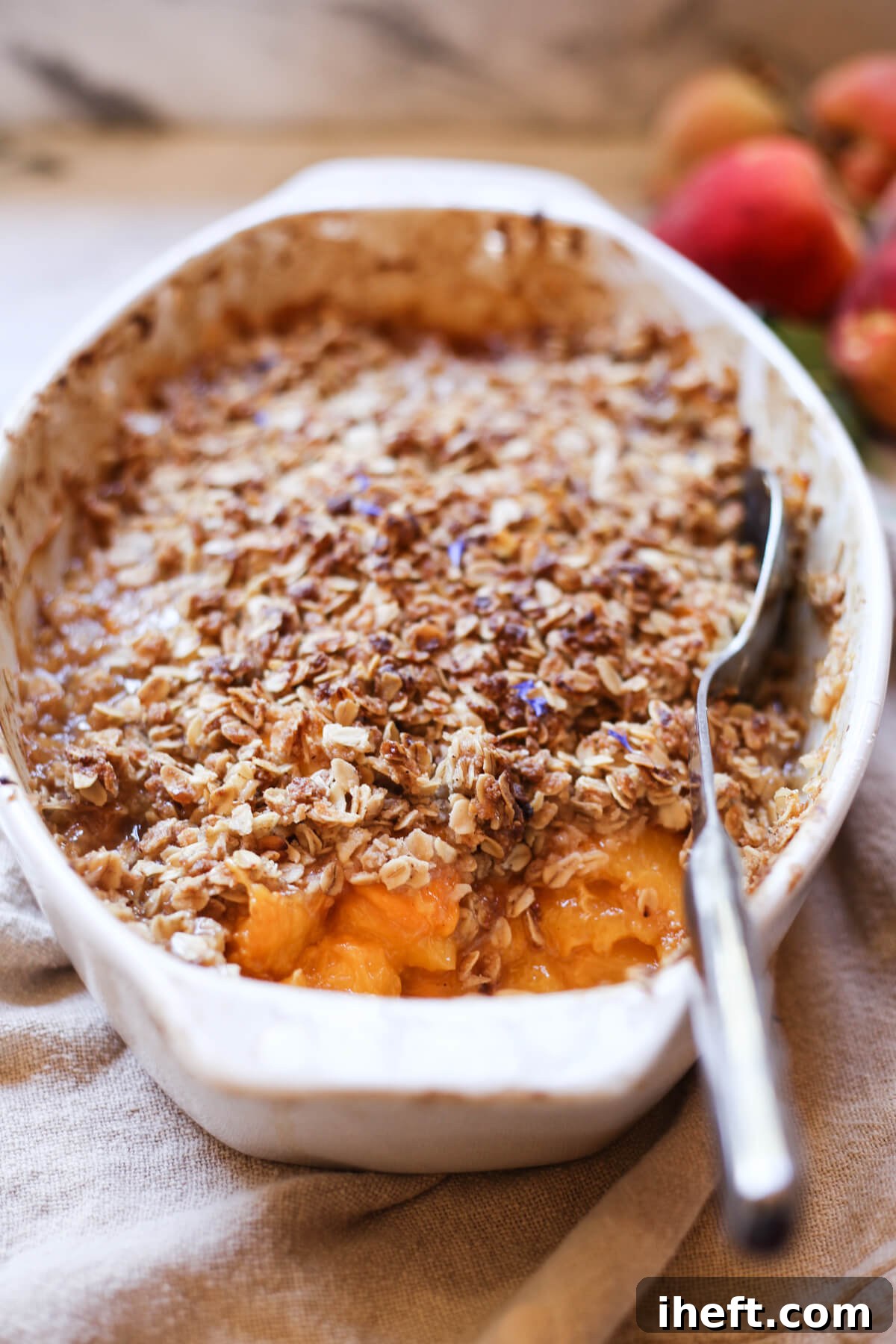 A white ceramic baking dish filled with a warm peach crisp made with fresh peaches and a golden oat topping, ready to be served.