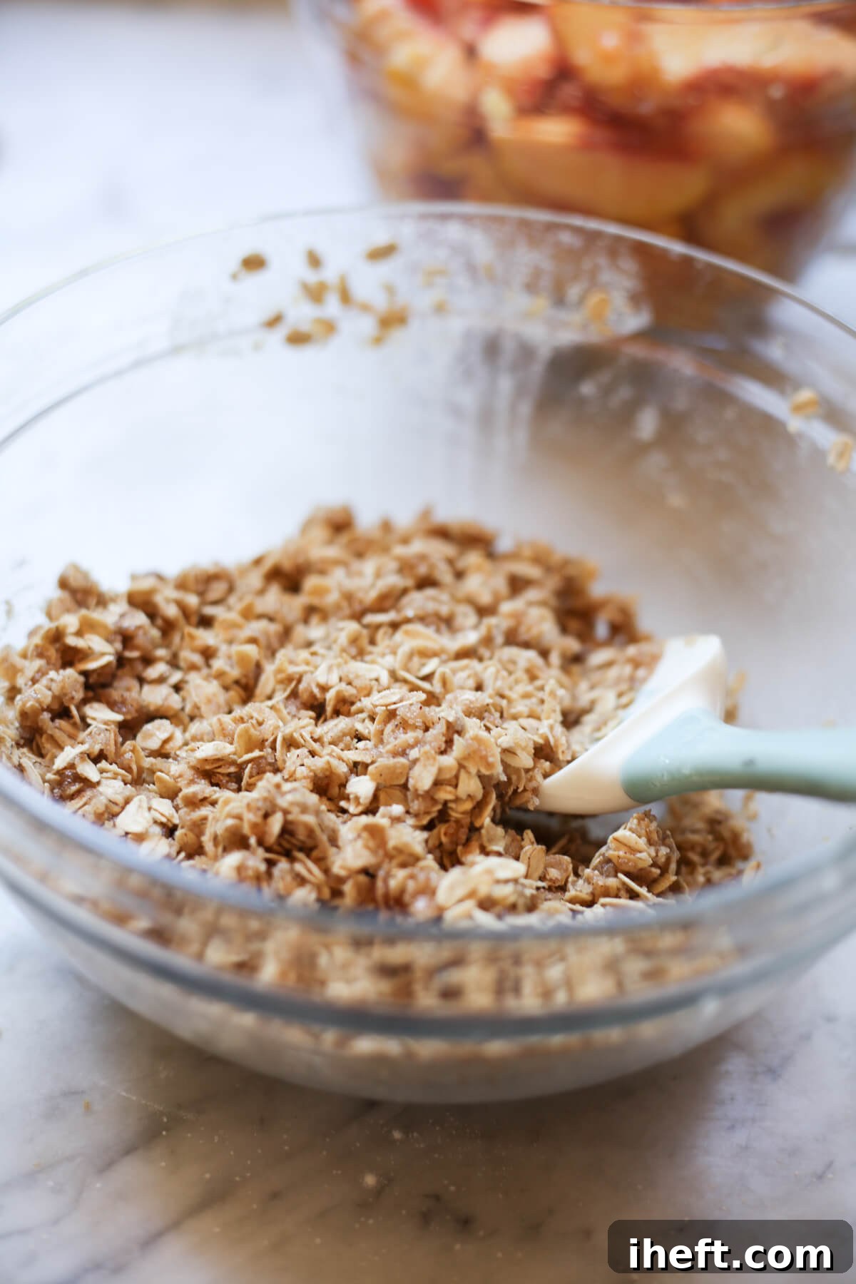 Oat crumble topping is mixed together with a rubber spatula in a glass bowl.
