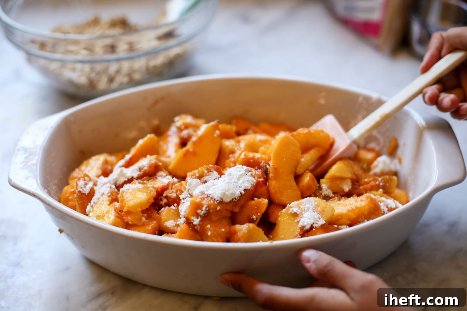 Sliced fresh peaches are gently tossed with cornstarch and brown sugar in a white casserole dish to make a peach crisp filling.