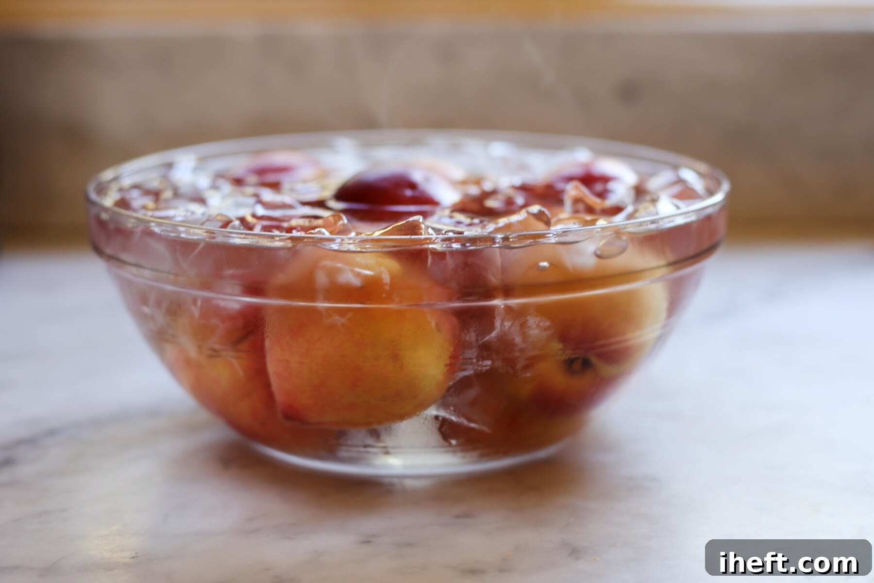 A glass bowl filled with ice, water, and hot peaches to blanch peaches for peeling. 