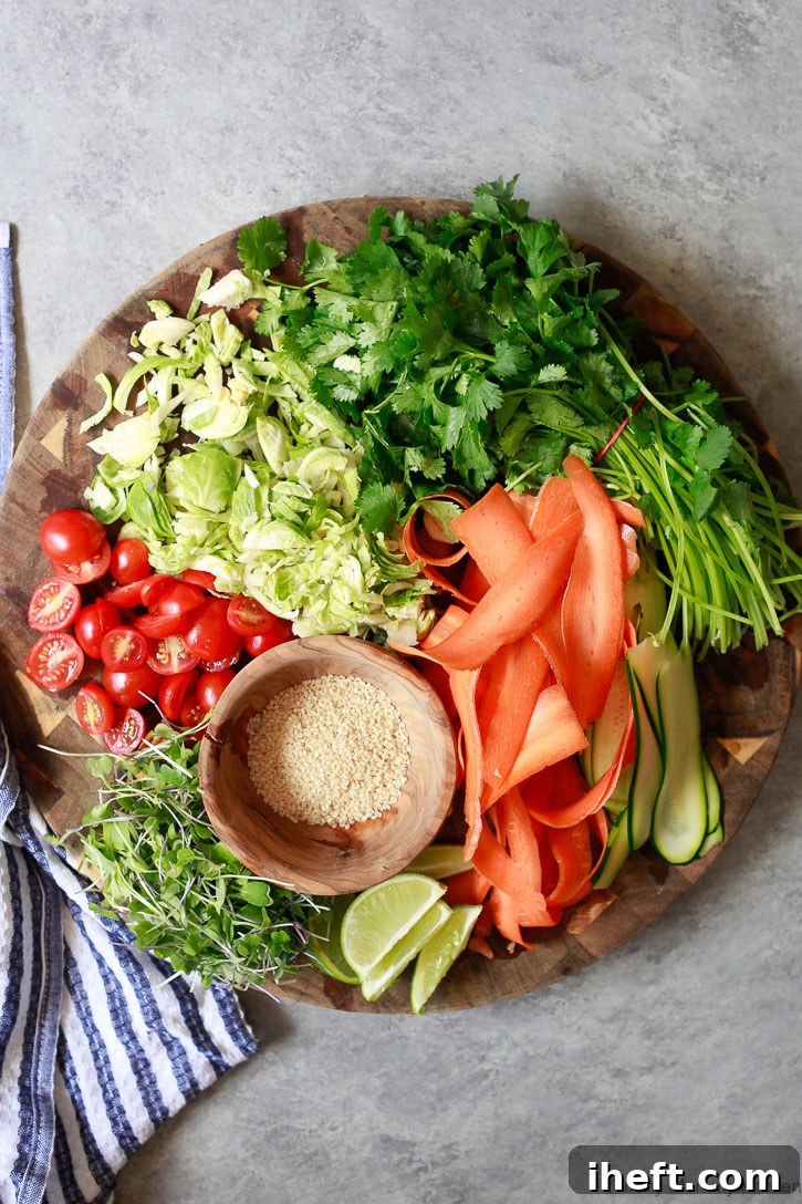 An array of fresh, vibrant topping ingredients for the Korean BBQ Chickpea Bowls, including carrot and zucchini ribbons, microgreens, tomatoes, cilantro, and sesame seeds.