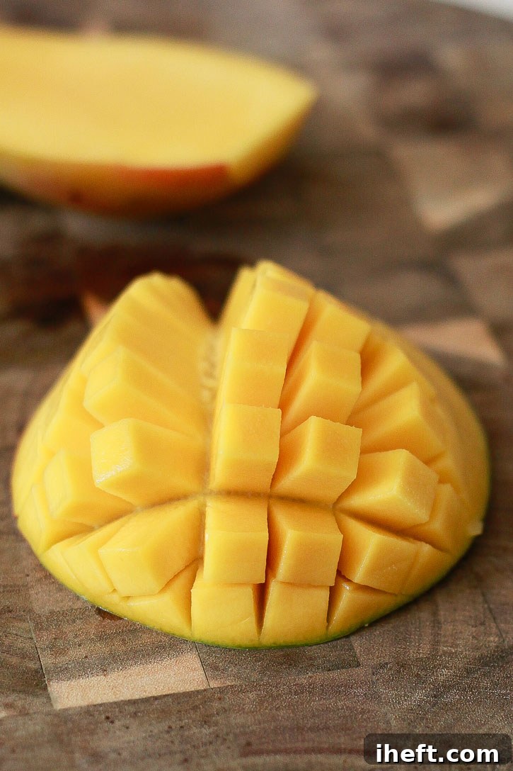 A close-up view of a mango half, meticulously scored in a grid pattern, demonstrating the 'hedgehog style' dicing technique, ready to have the cubes scooped out.