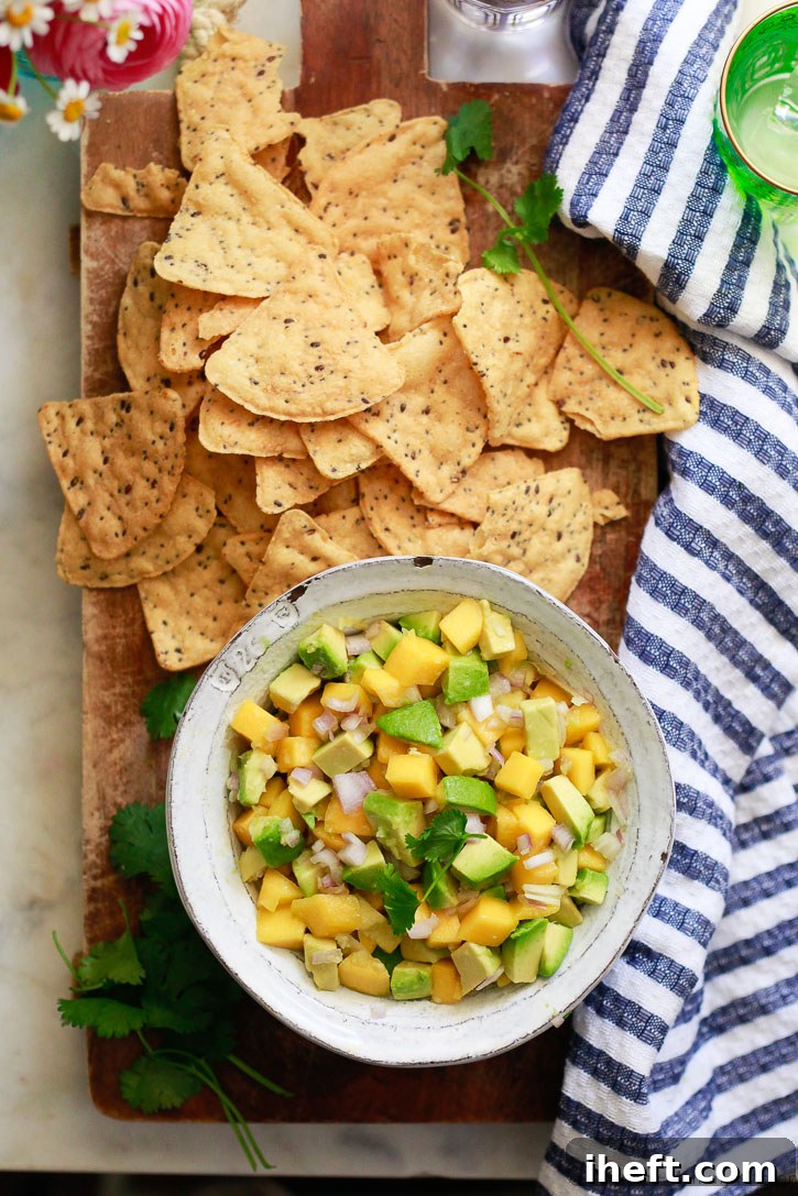 A beautifully presented bowl of fresh homemade mango avocado salsa, accompanied by a generous portion of flax chips, highlighting the vibrant colors and appealing texture of the healthy dip.