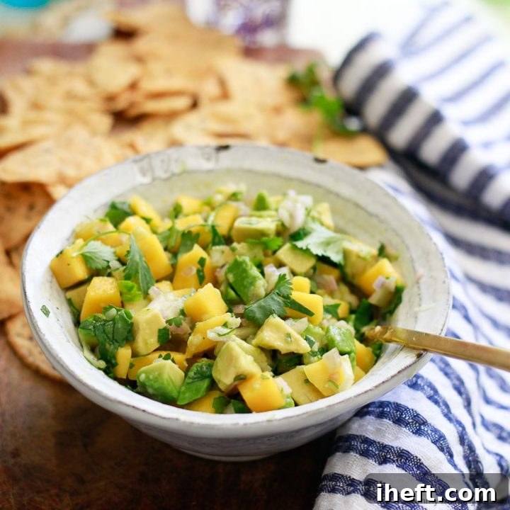 A vibrant bowl of fresh mango avocado salsa, brimming with colorful diced mango, creamy avocado, and aromatic herbs, served with a side of crispy tortilla chips, inviting you to dig in.