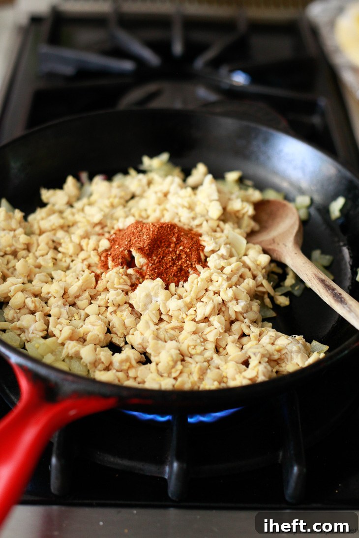 Tempeh being cooked with onions and taco seasoning in a skillet, transforming into a savory filling for tempeh tacos.