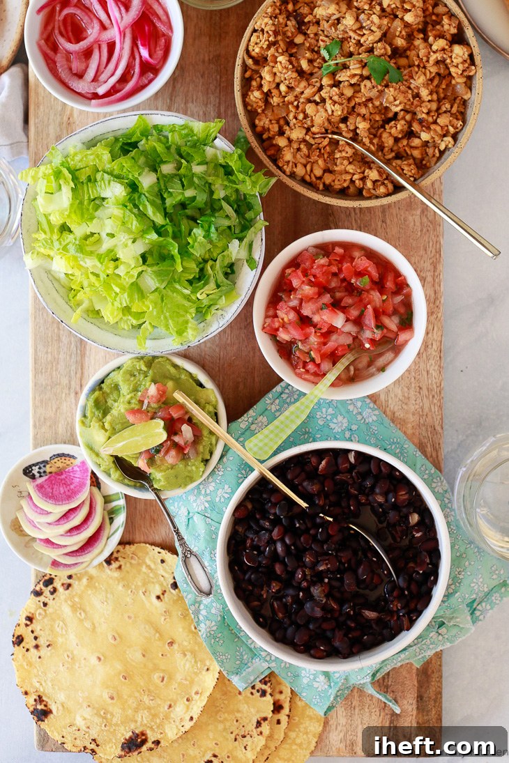 A vibrant spread of tempeh taco filling, black beans, salsa, creamy guacamole, and fresh lettuce arranged beautifully on a long serving board, perfect for a DIY taco bar.