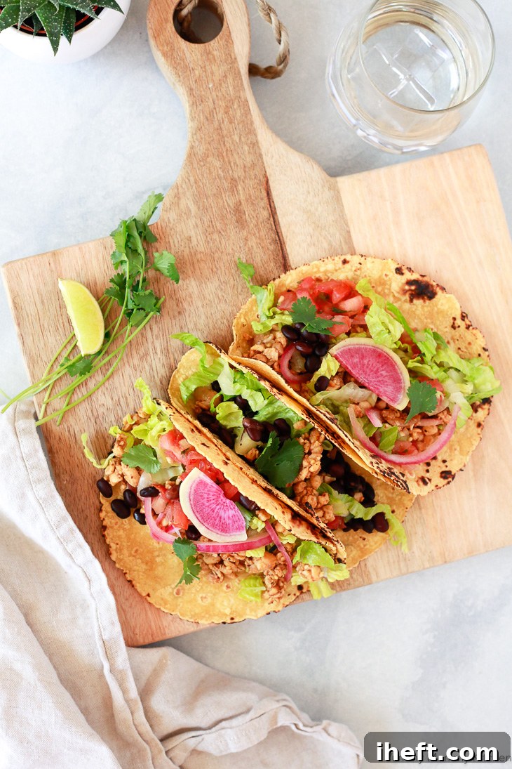 Three visually appealing vegan tacos filled with savory tempeh, hearty black beans, crisp lettuce, and garnished with colorful watermelon radish slices.