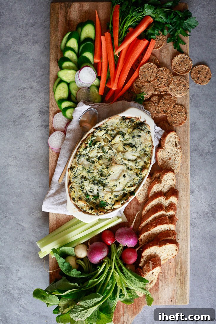A beautiful crudite platter with vegan baked spinach artichoke dip, vegetables, crackers, and baguette. This dip is so delicious for a vegan and paleo appetizer. 