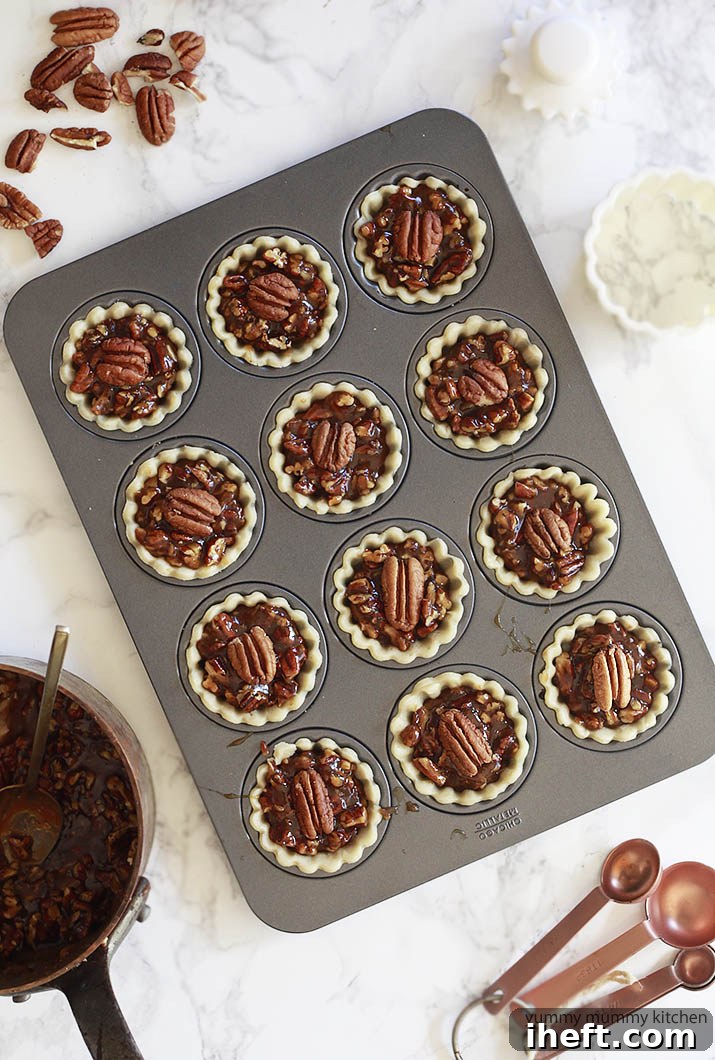 A trio of miniature pecan pies, baked in a mini tart pan, sits elegantly on a pristine white marble countertop, showcasing portion-controlled delight.