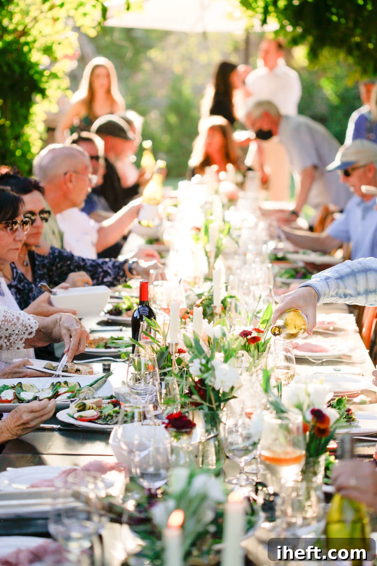An elegantly set outdoor Thanksgiving table, adorned with lush greenery, vibrant orange and red flowers, and gleaming brass candlesticks, ready for a festive gathering with guests enjoying wine and conversation.