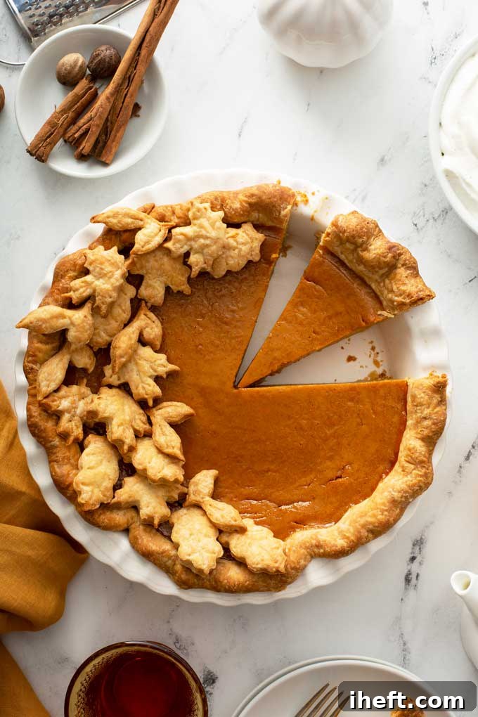 A perfectly baked pumpkin pie, intricately decorated with delicate pie crust leaves, sits invitingly on a pristine marble counter, ready for a Thanksgiving feast.