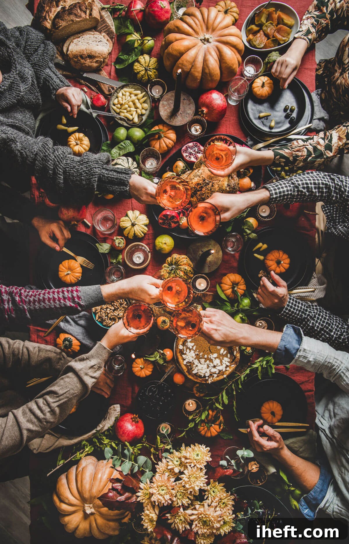An inviting overhead view of guests raising wine glasses around a beautifully arranged traditional holiday table, featuring rich Thanksgiving colors, festive pumpkins, and a classic red tablecloth.