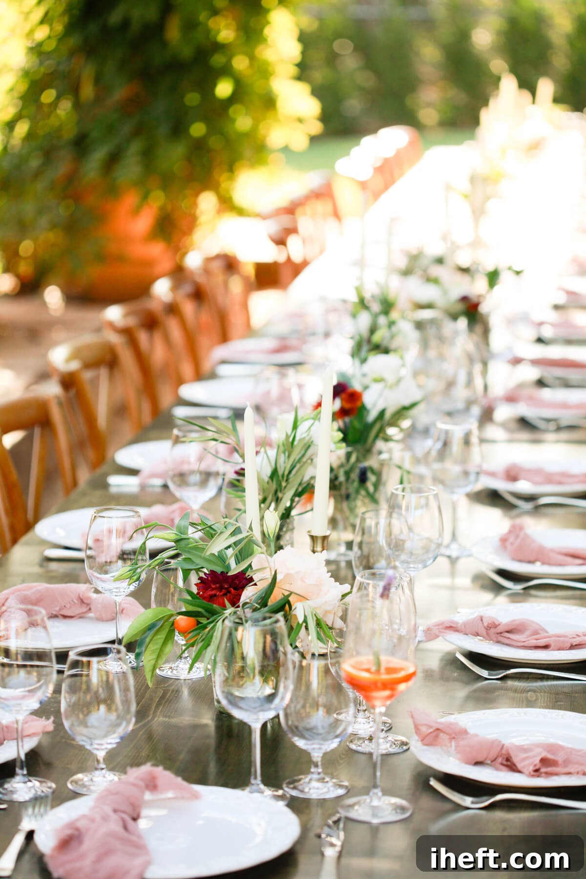 An enchanting outdoor table setup adorned with delicate blush napkins, gleaming brass candlestick holders, and a vibrant floral arrangement featuring red, blush, green, and orange flowers, creating a modern and romantic Thanksgiving ambiance.