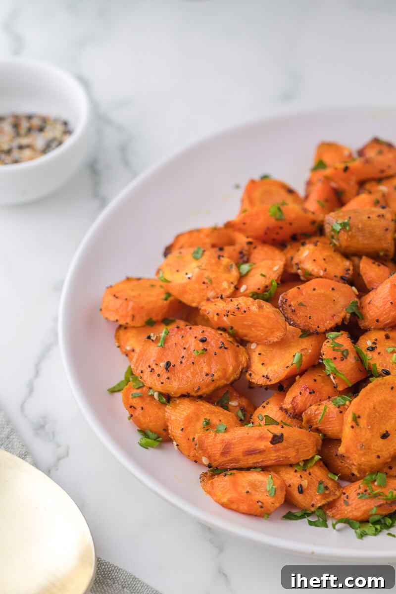 A bowl of perfectly cooked, glazed air fryer carrots on a light marble countertop, garnished with fresh herbs.