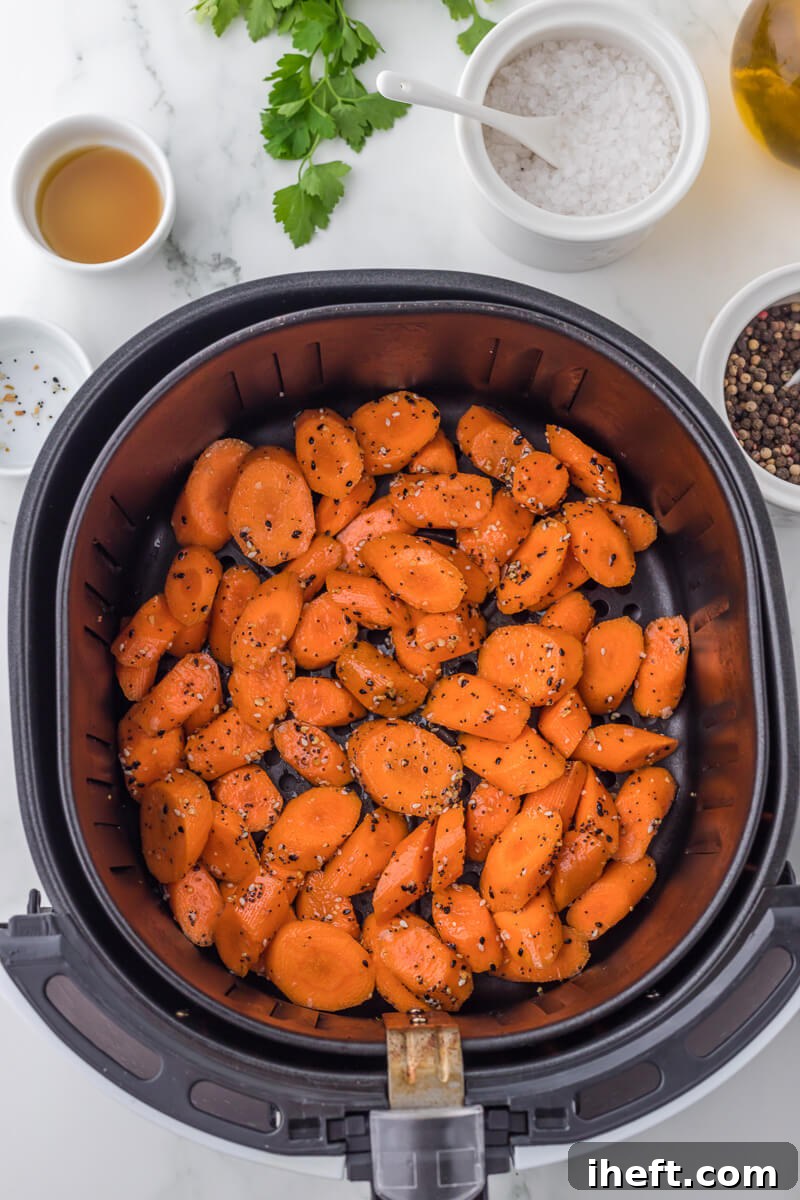 Carrot slices and seasonings in the basket of an air fryer.