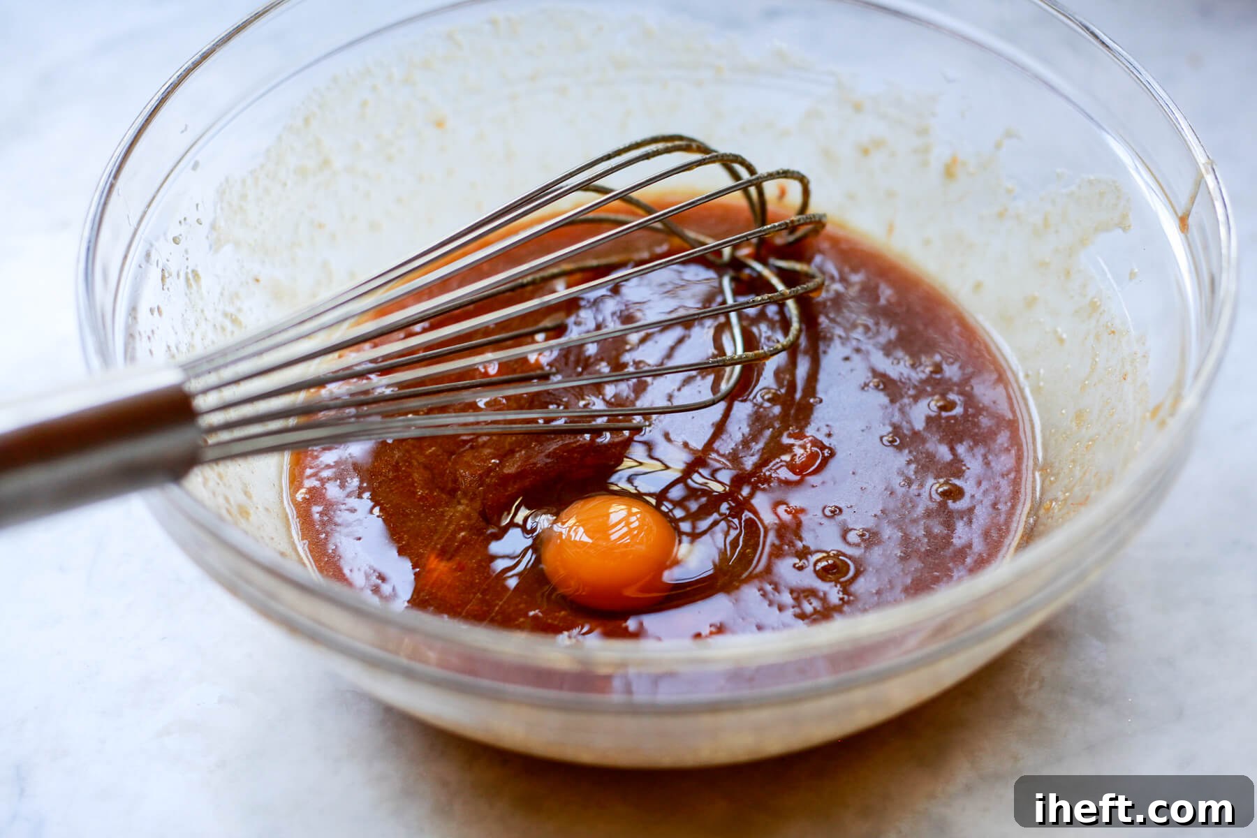 An egg is carefully cracked and added to the creamy wet ingredients for persimmon bread, ready to be beaten in.