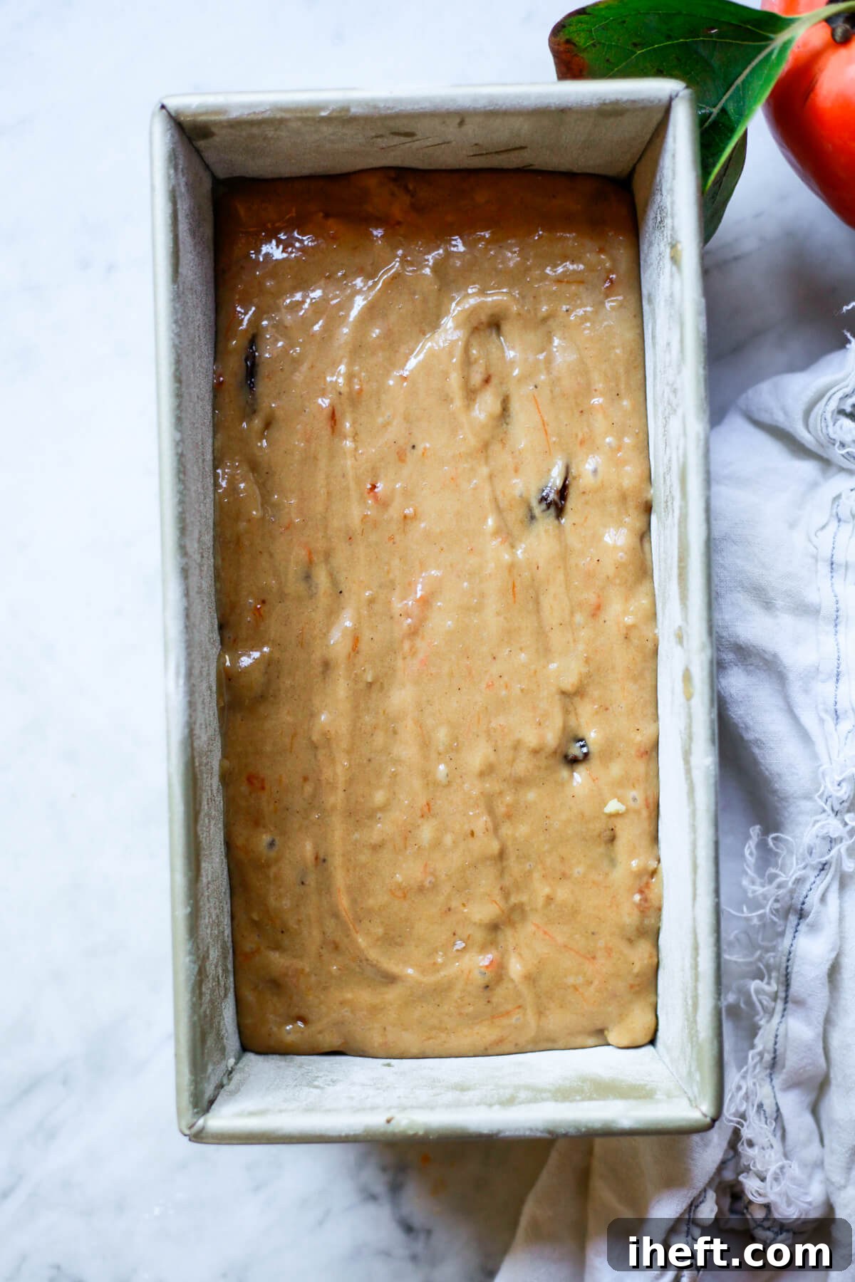 Lush persimmon bread batter fills a prepared loaf pan, smoothed out and ready for the oven.