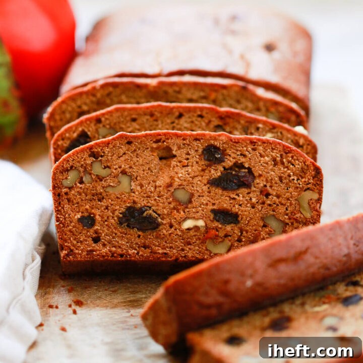 A perfectly baked loaf of persimmon bread, sliced to reveal plump raisins and crunchy walnuts, rests on a wooden cutting board.