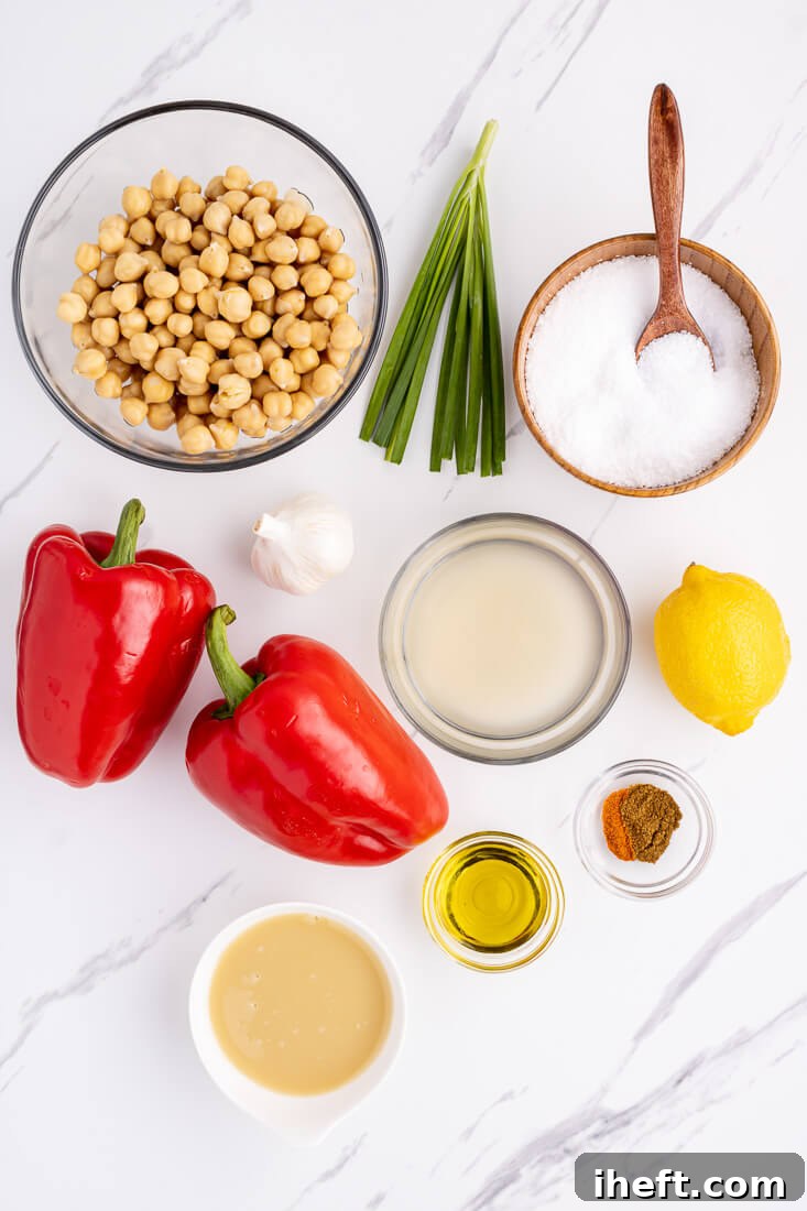 The ingredients for roasted red pepper hummus on a marble countertop. These include chickpeas, salt, garlic, red bell peppers, olive oil, tahini, lemon, and spices.