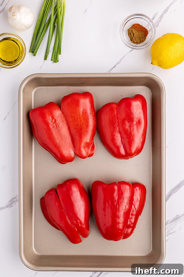 Two red bell peppers, halved, on a roasting pan.