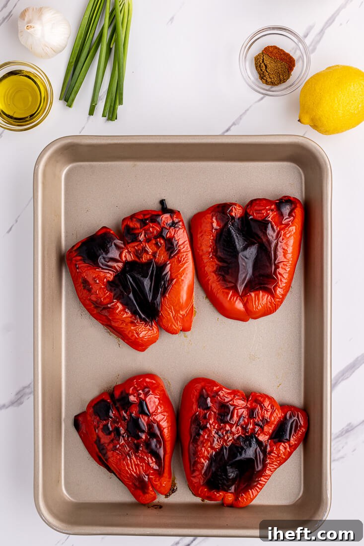 2 blistered roasted red peppers on a sheet pan.