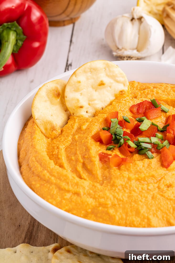 Roasted red pepper hummus in a bowl garnished with chopped roasted red pepper and chives.
