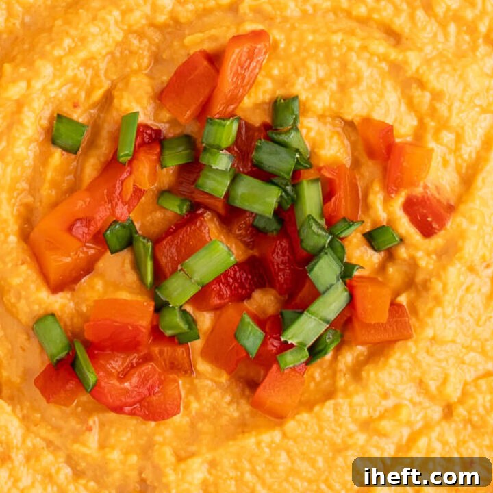 A close up photo of roasted red pepper hummus topped with chopped red peppers and green onions.