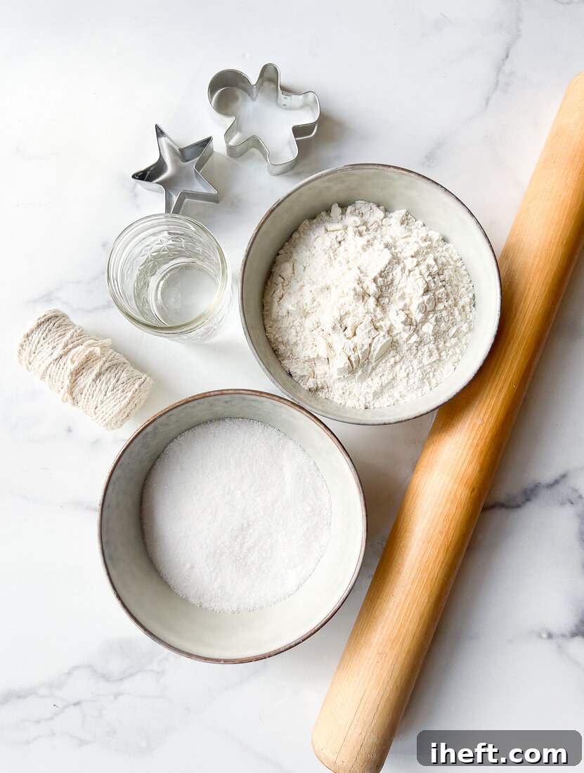 Bowls of flour, salt, and water sit on a countertop next to a wooden rolling pin and two cookie cutters. These are the ingredients for salt dough. 