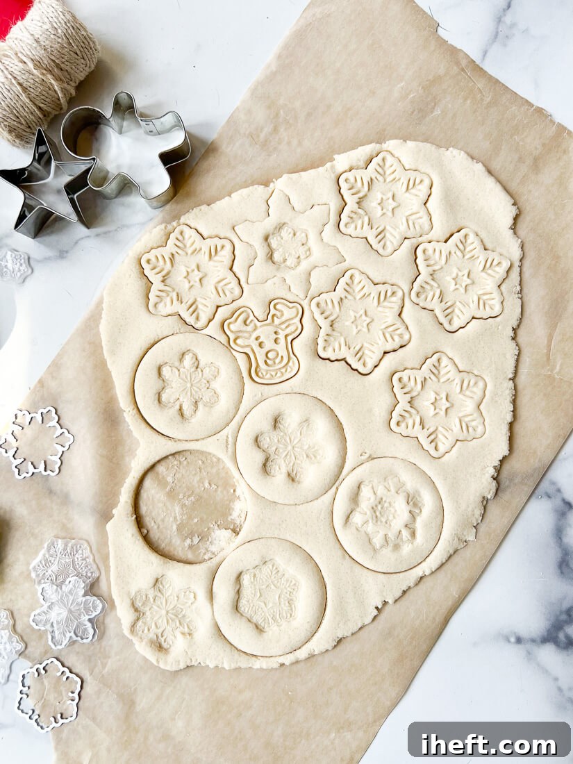 Salt dough pressed into Christmas shapes with cookie cutters on a piece of parchement paper on a marble counter. 