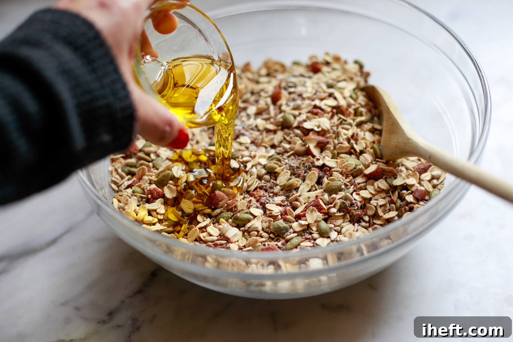 A small bowl of olive oil is poured over the dry ingredients for adventure seed bread.